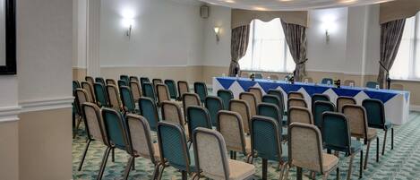 Un salón de conferencias con filas de sillas, una larga mesa con mantel azul y una alfombra estampada.