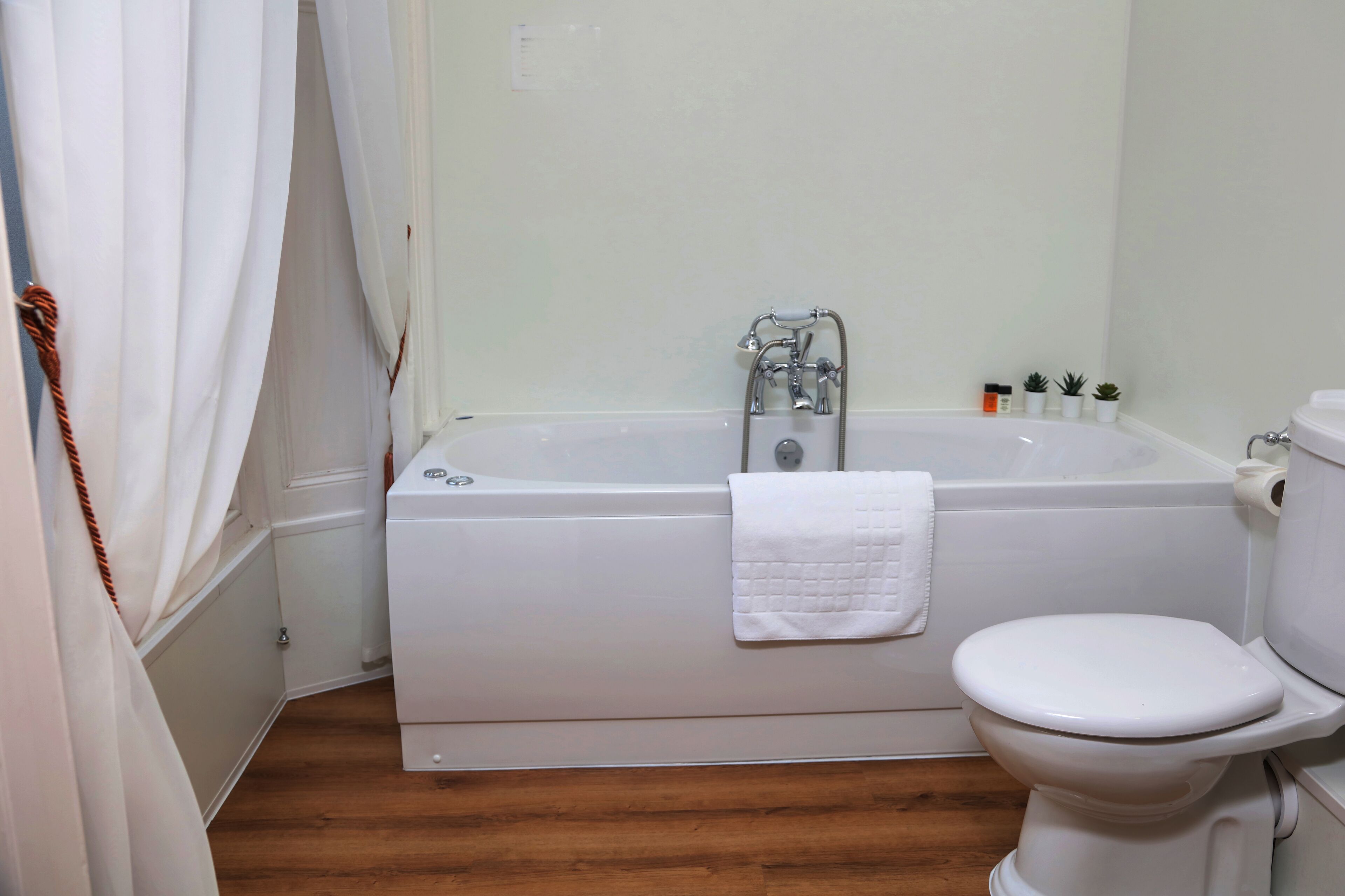 A bathroom with a bathtub, toilet, and a wooden floor.