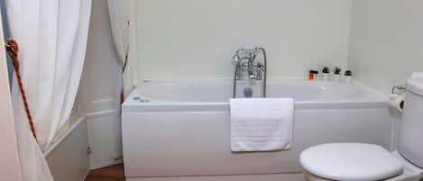 A bathroom with a bathtub, toilet, and a wooden floor.