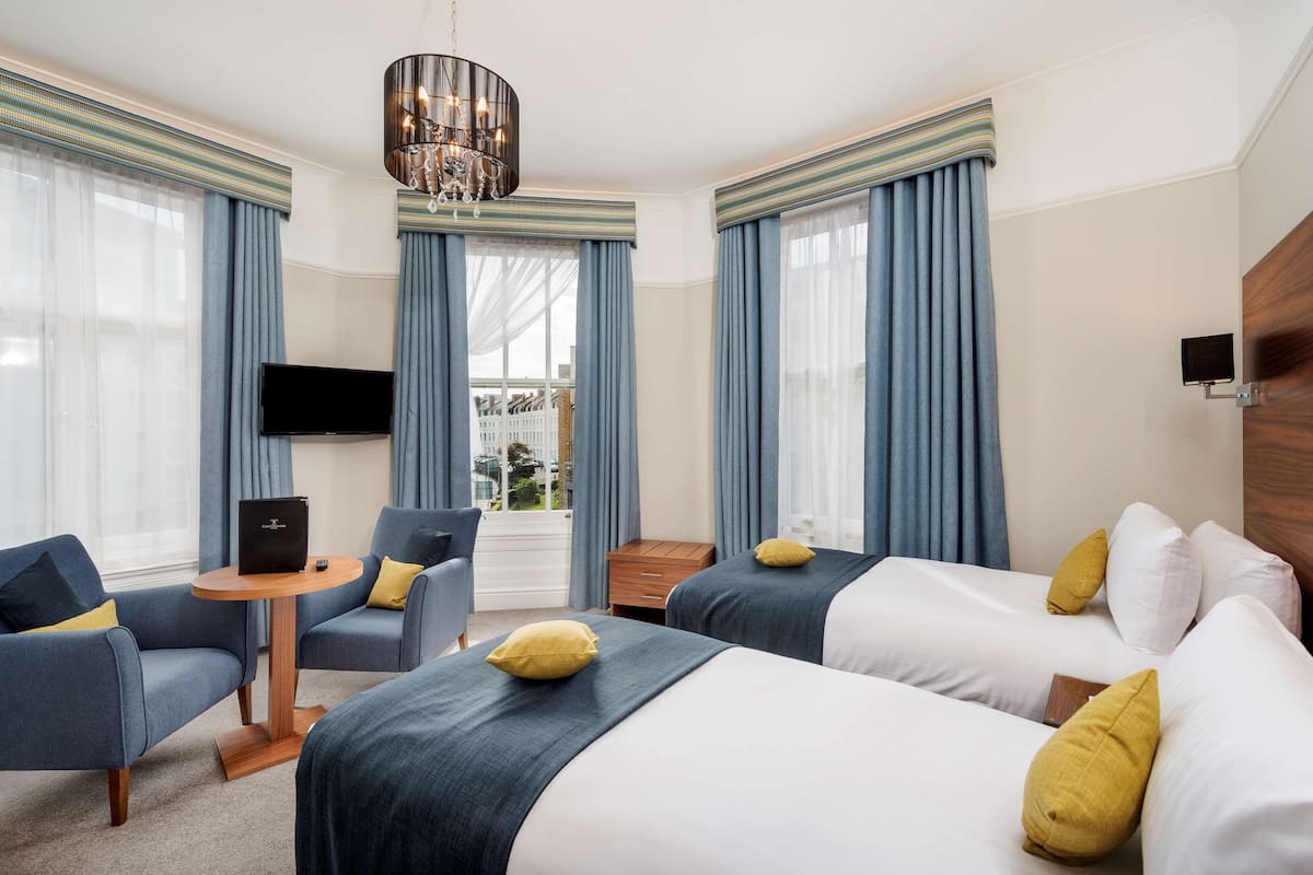 Ein Hotelzimmer mit zwei Betten, einem Fernseher, einem Holznachttisch und Blick ins Freie.