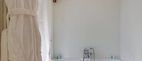 A bathroom with a bathtub, toilet, and a robe hanging on the wall.