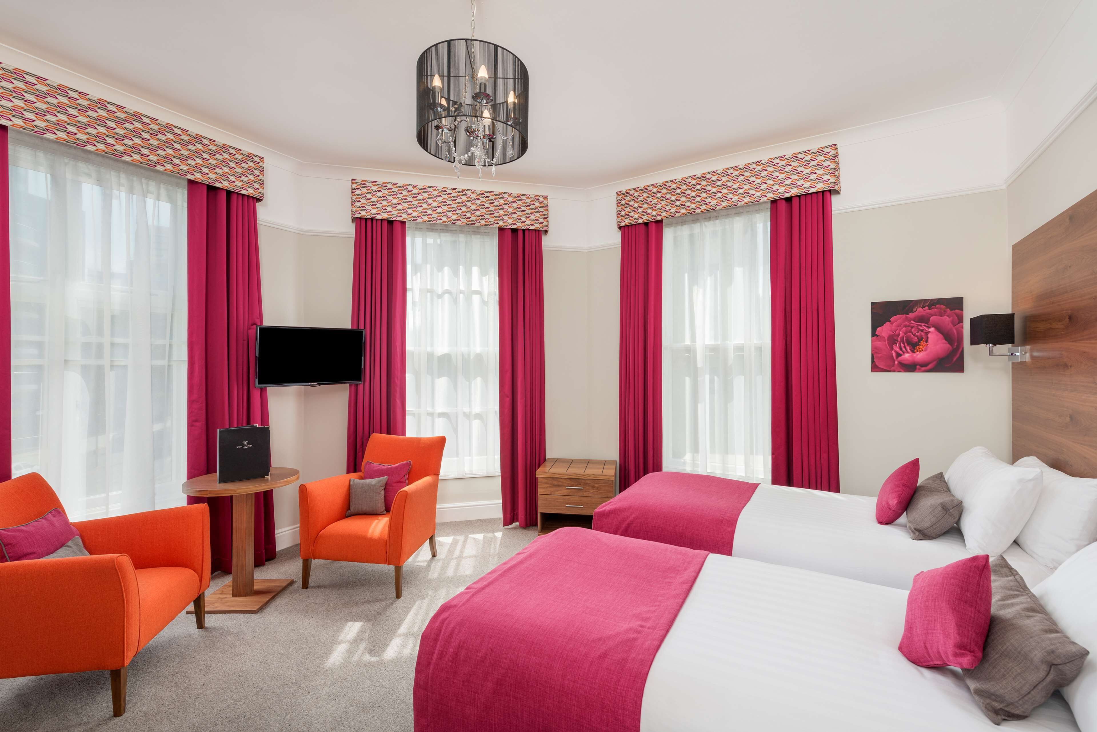 A hotel room with two beds, a TV, a small table, and orange chairs.