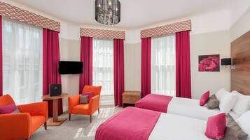 A hotel room with two beds, a TV, a small table, and orange chairs.