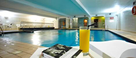 A swimming pool area with a book and a glass of orange juice on a white table.