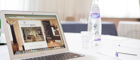 Valkoisella pöydällä on MacBook Air -läppäri, vesipullo, lasi vettä ja kynä.