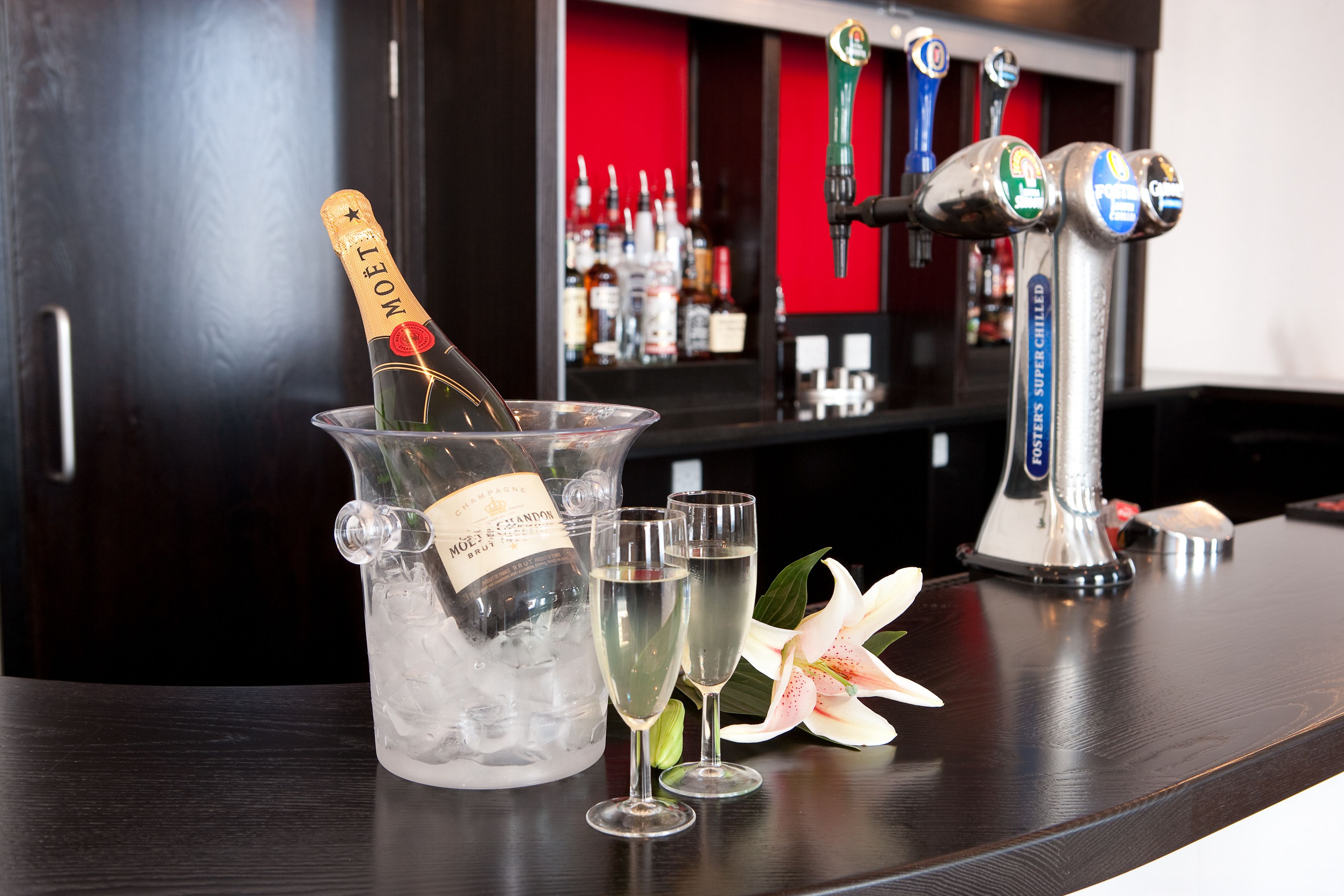 Eine Bar mit einer Moët Champagnerflasche, zwei Sektgläsern und einer Blume auf einer Holztheke.