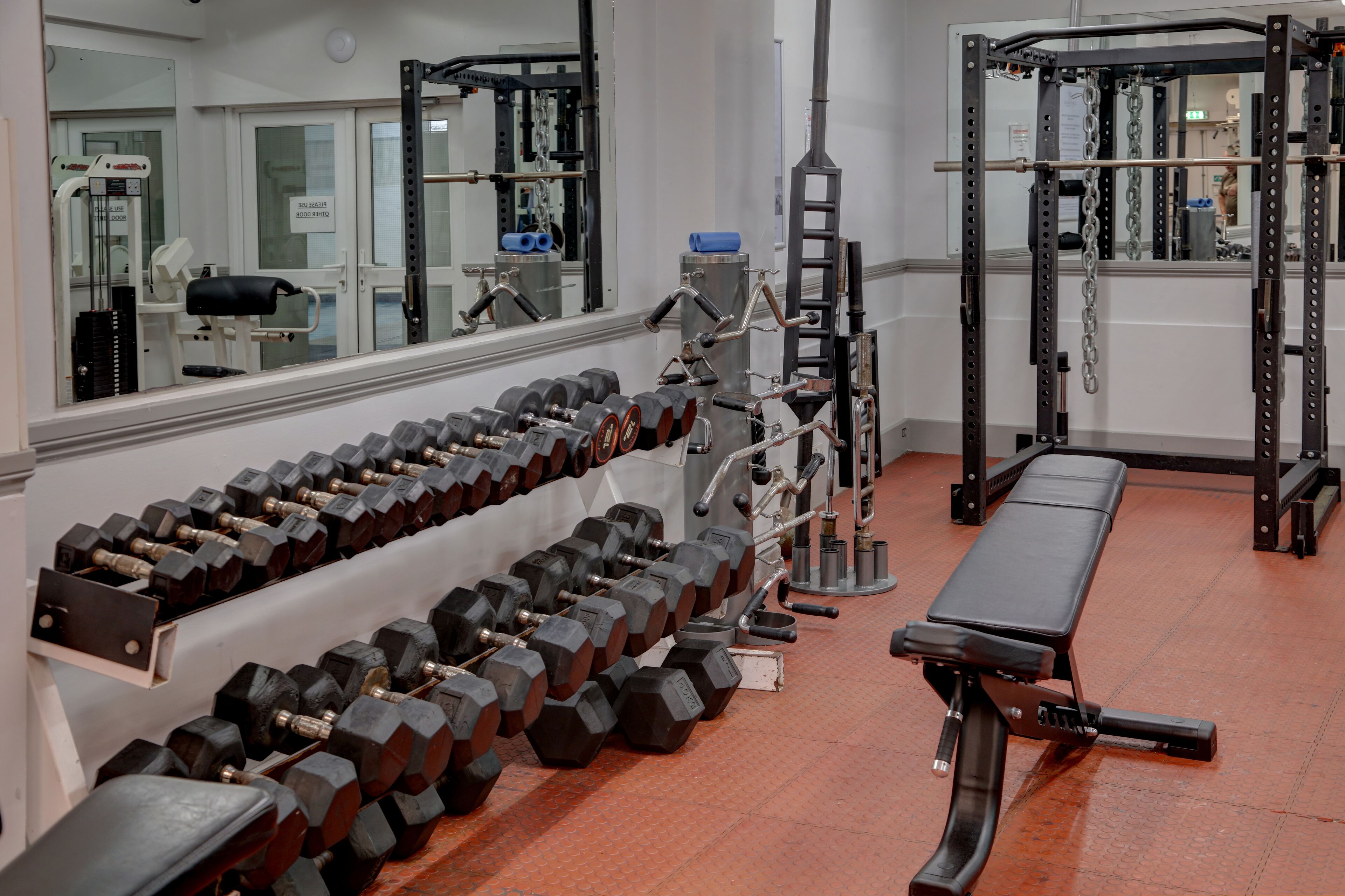 A gym with weightlifting equipment, benches, and a mirrored wall.