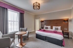 A modern hotel room with a large bed, two bedside tables, a round table, and a sofa.