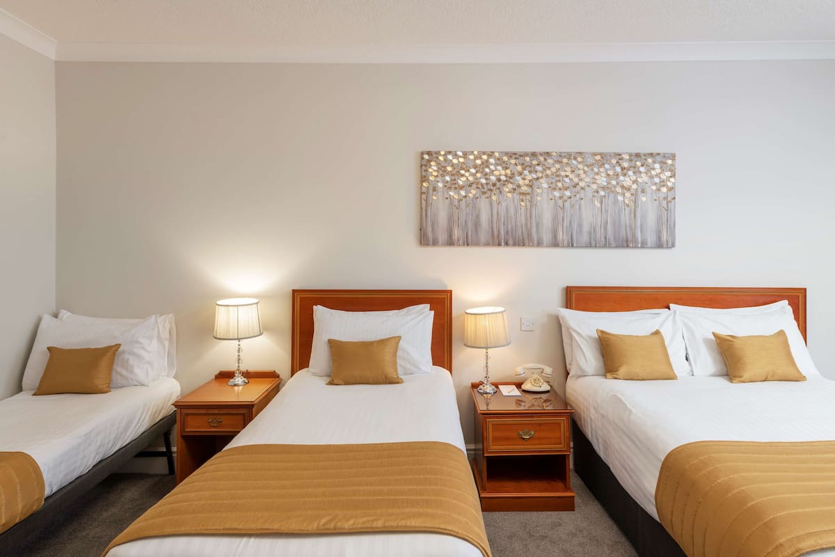 Ein Hotelzimmer mit zwei Einzelbetten, jeweils mit einem Holzkopfende, weißer Bettwäsche und einer braunen Tagesdecke. An den Nachttischen stehen Lampen und ein Telefon. Darüber hängen die Betten ein dekoratives Wandbild.