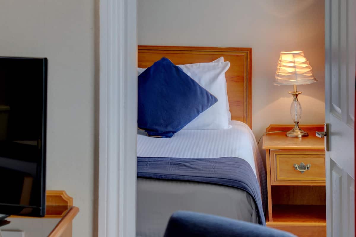 Ein Hotelzimmer mit Bett, Nachttischlampe und Fernseher auf einer Holzkommode.