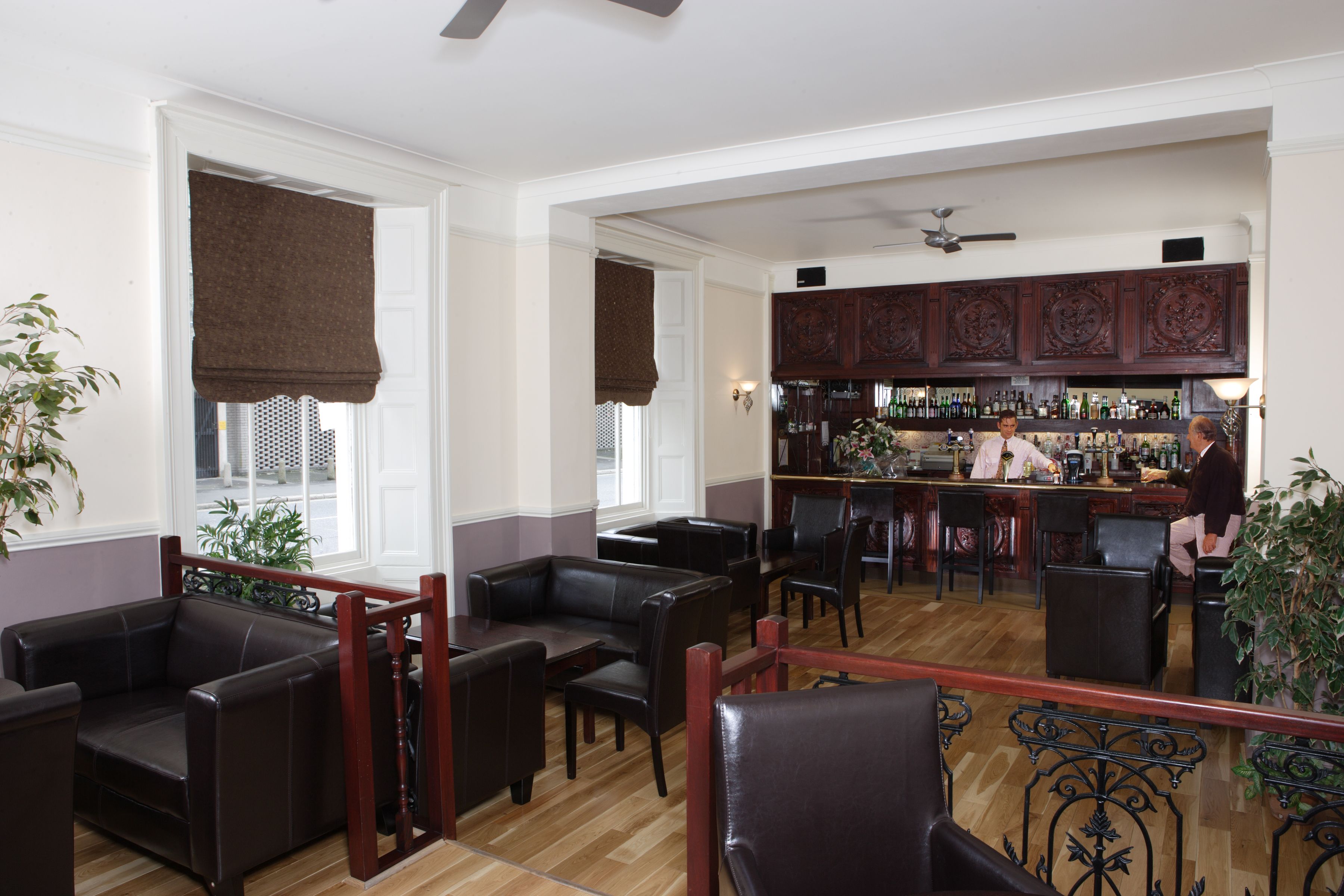 Una zona de bar con armarios de madera y un camarero. Hay sillones de cuero y suelo de madera.