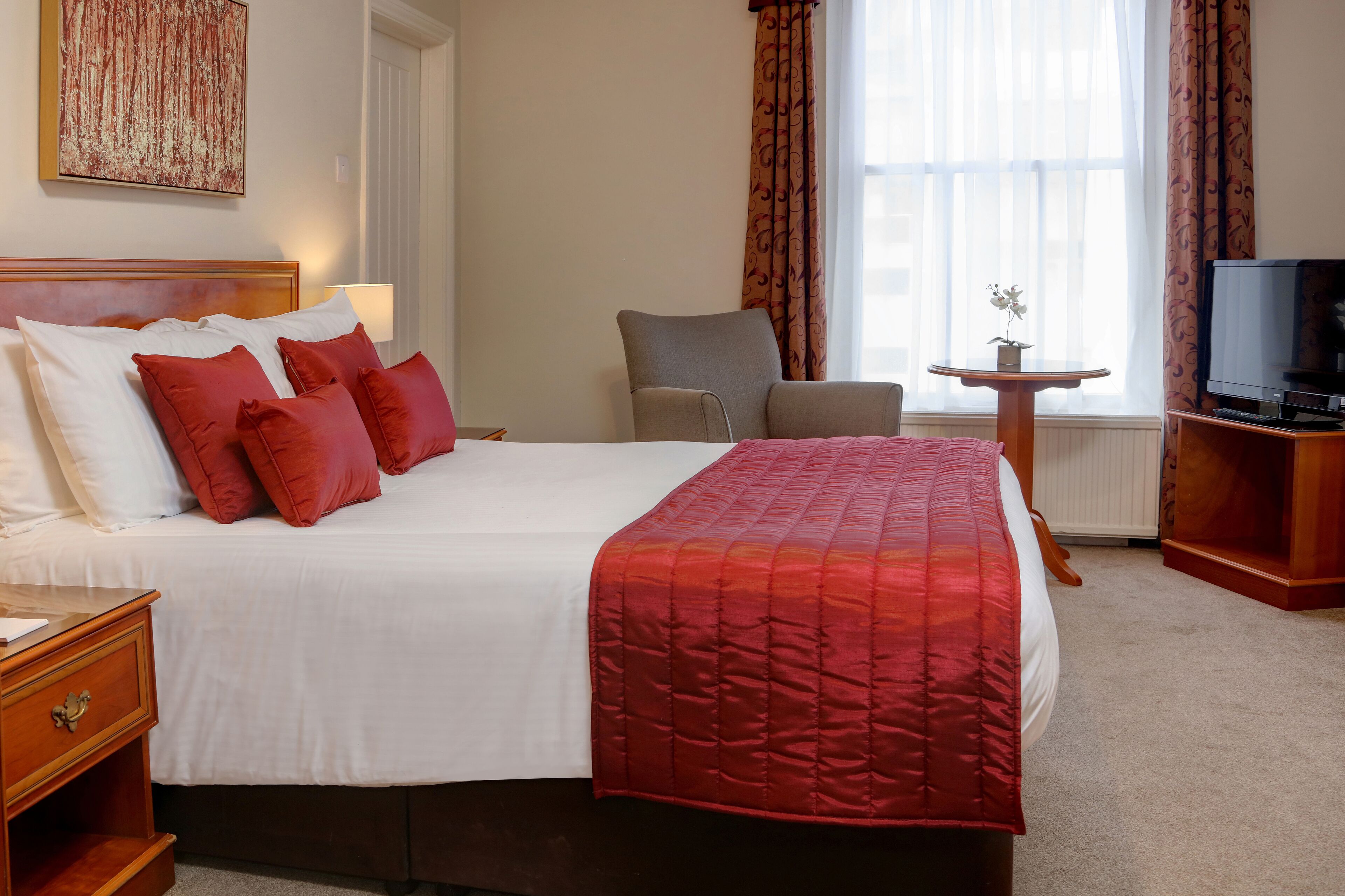 A hotel room with a large bed, a chair, a television, and a small table with a flower.