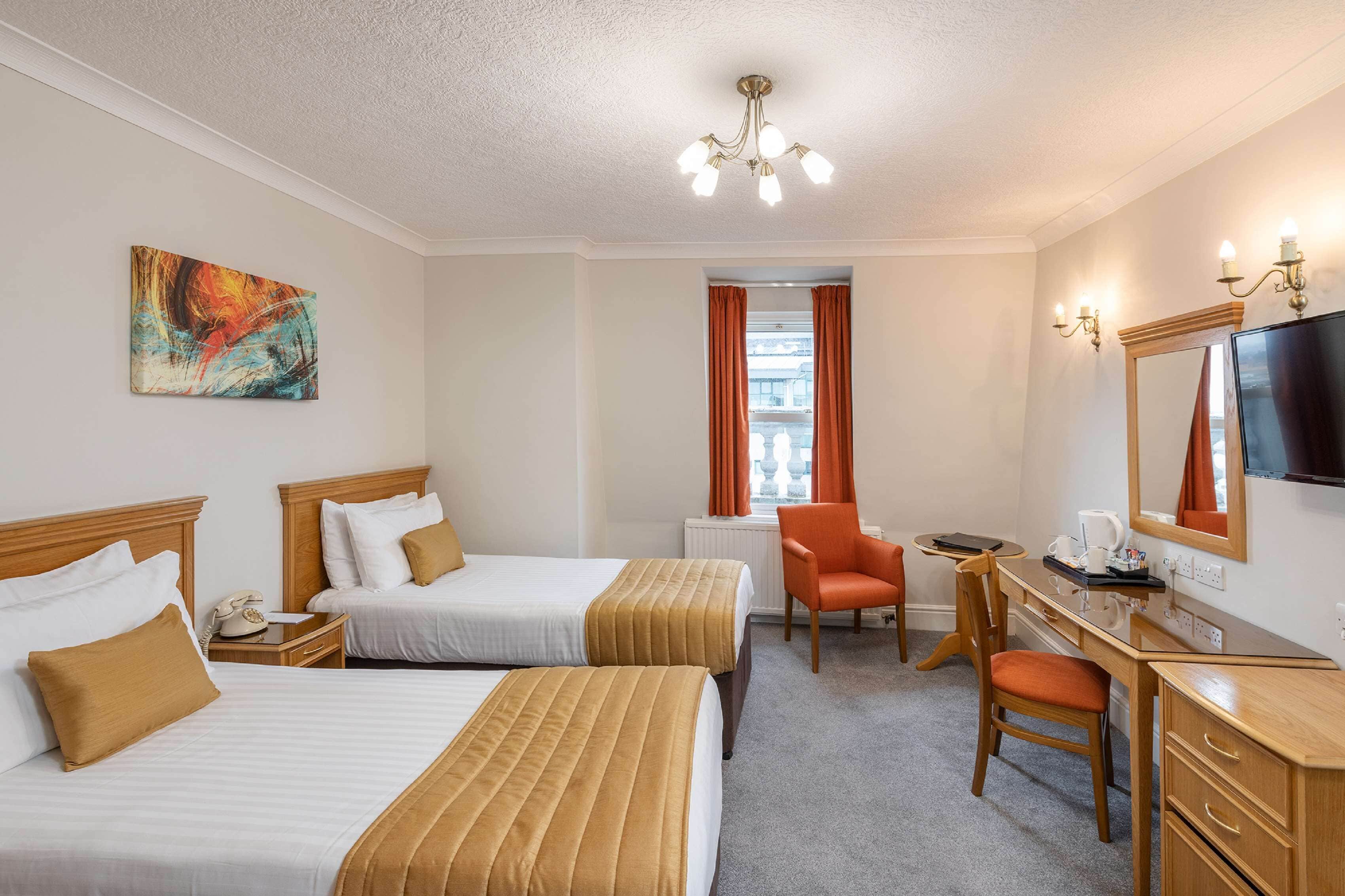 Habitación de hotel con dos camas, un escritorio, una silla, un televisor y un cuadro en la pared.