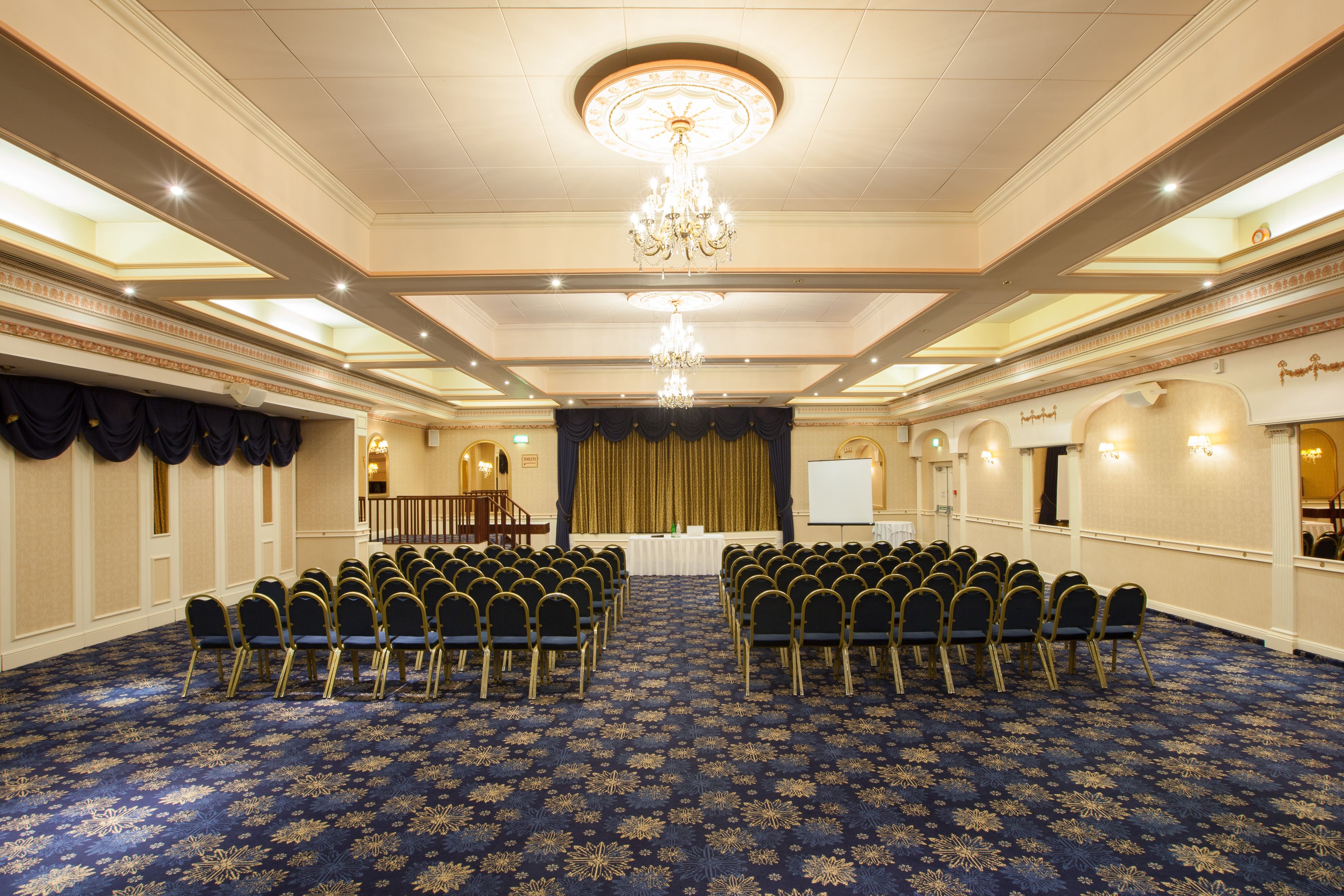 A conference room with rows of chairs, a stage with a whiteboard, and a chandelier.