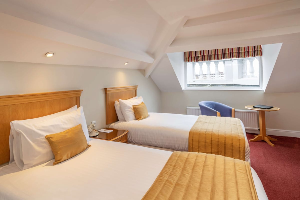 Ein Hotelzimmer mit zwei Betten, einem kleinen Tisch, einem Sessel und einem Fenster mit Blick.