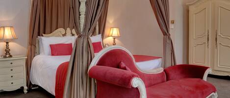 A four-poster canopy bed with red and white bedding, two bedside lamps, and a red upholstered chair.