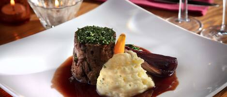 Un plato blanco con un bistec cubierto de hierbas, puré de papas y una zanahoria.
