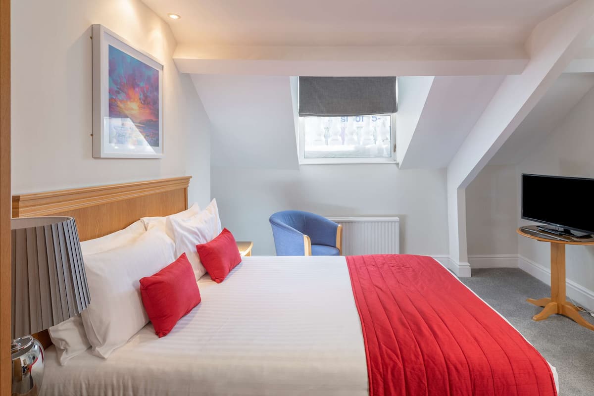 Ein Hotelzimmer mit einem großen Bett, einem Schreibtisch mit Fernseher, einem Sessel und einem Fenster mit Blick.