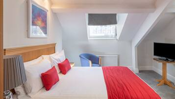 Habitación de hotel con una cama grande, un escritorio con televisor, una silla y ventana con vistas.