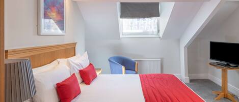 A hotel room with a large bed, a desk with a television, a chair, and a window with a view.