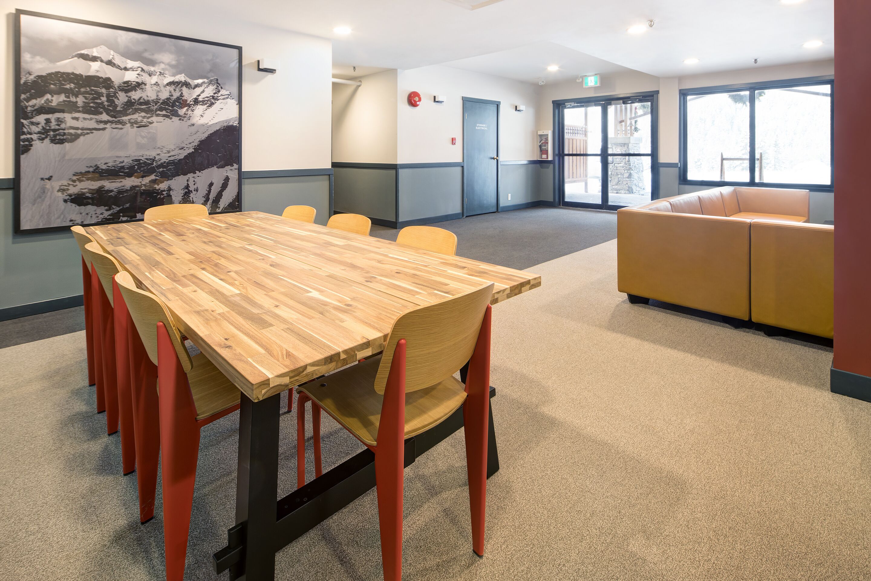 A conference room with a wooden table, orange chairs, a large wall painting, and a yellow sofa.