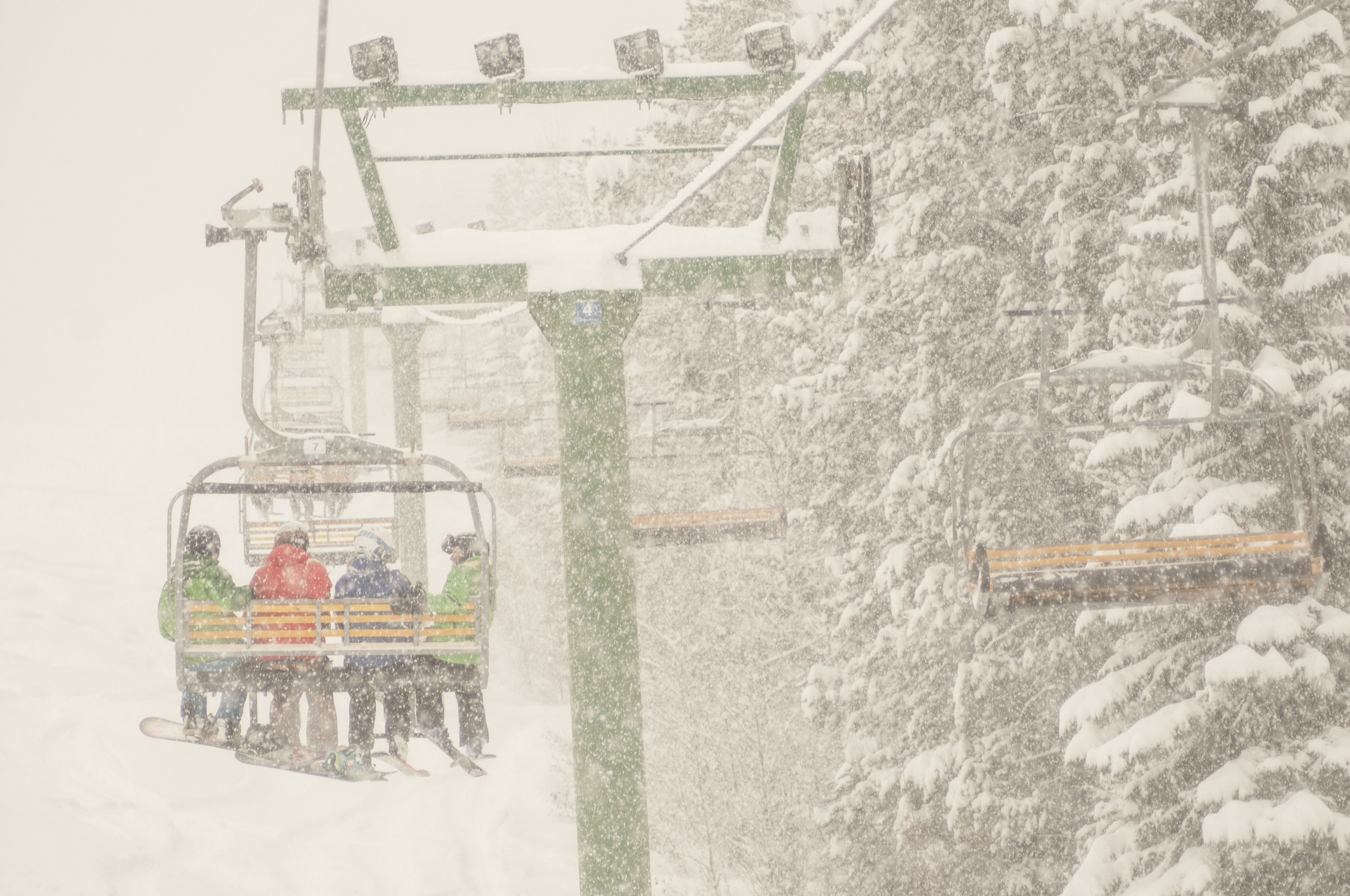 A ski lift with passengers, surrounded by snow-covered trees.