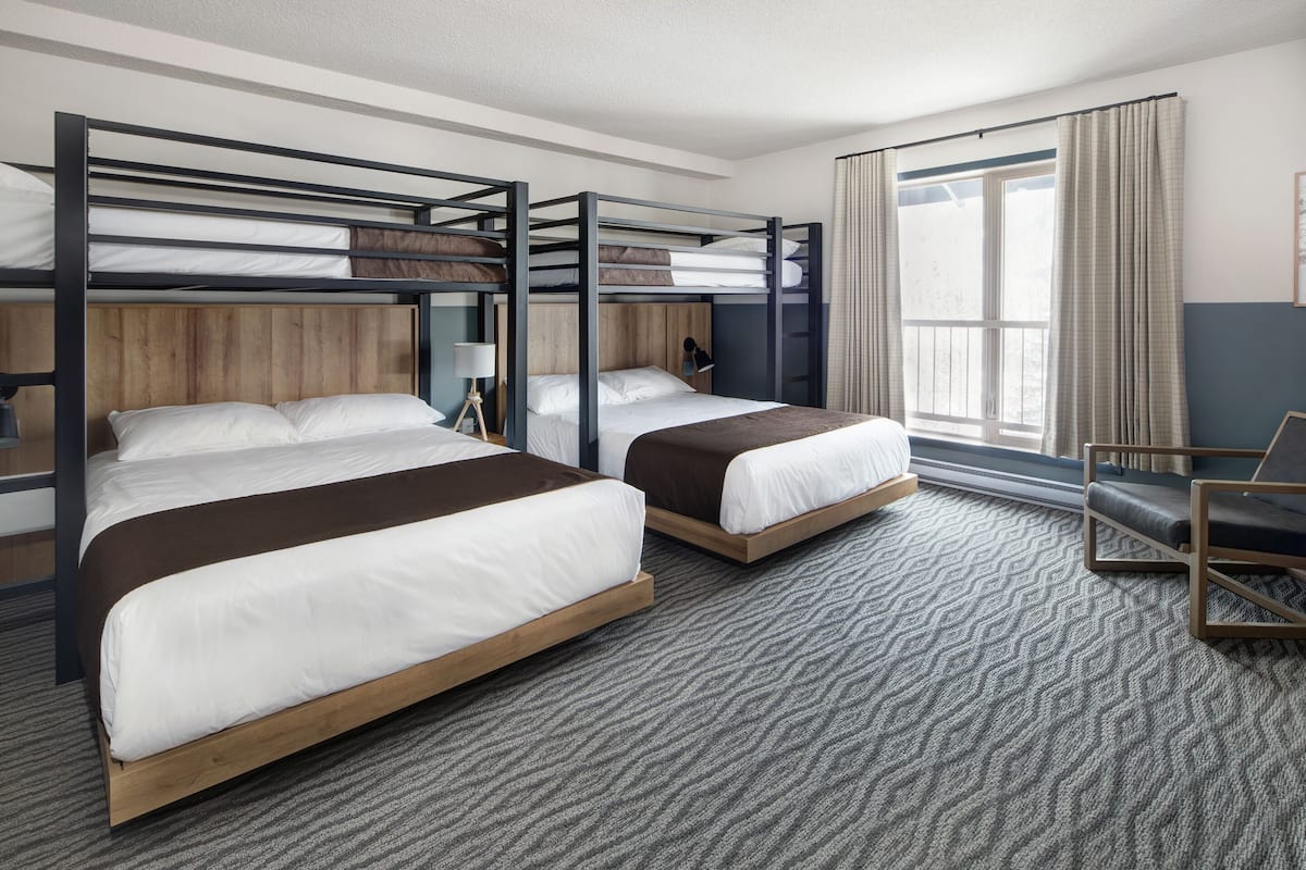 A hotel room with two bunk beds, a desk, a chair, and a large window with curtains.