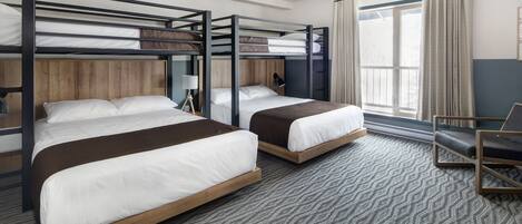 Ein Hotelzimmer mit zwei Etagenbetten, einem Schreibtisch, einem Stuhl und einem großen Fenster mit Vorhängen.
