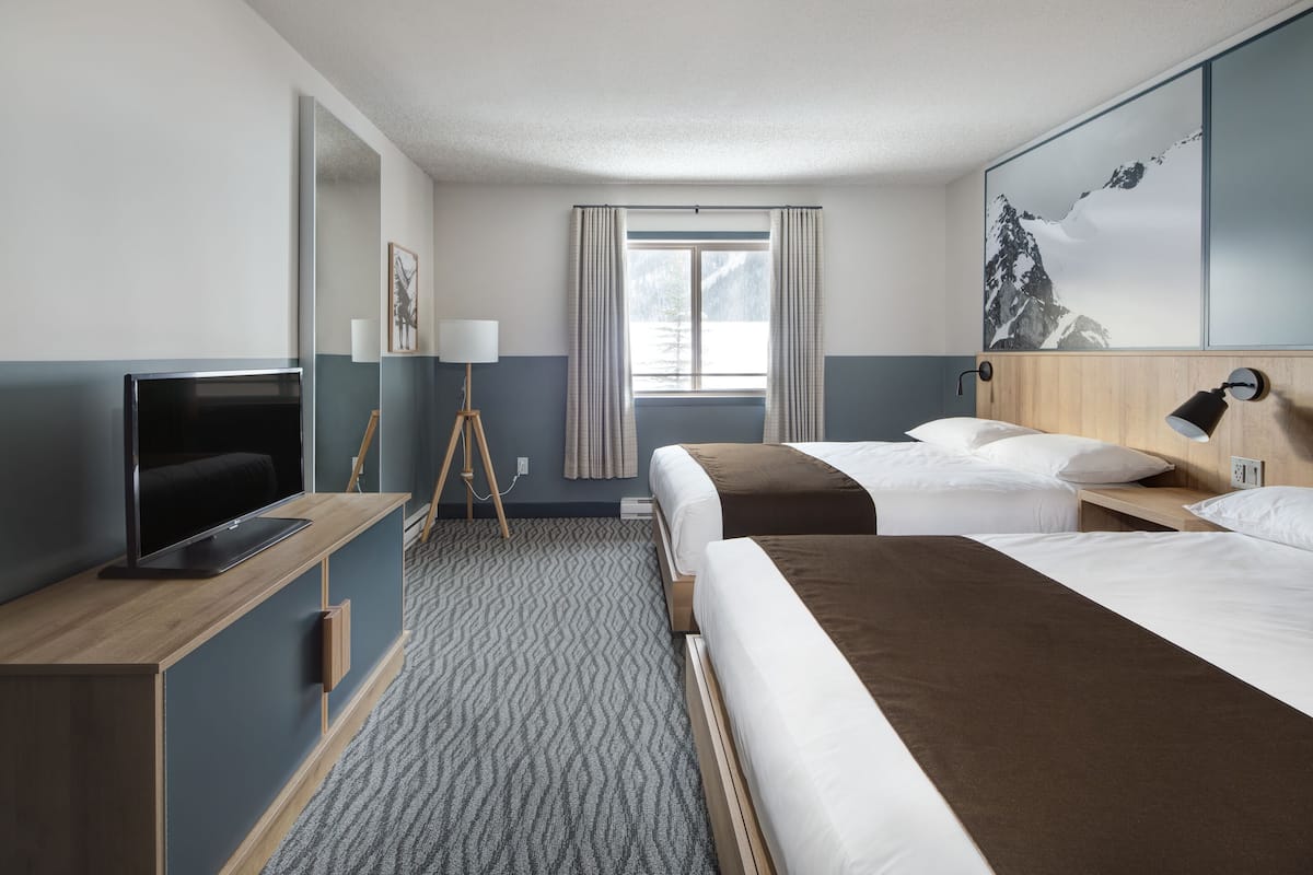 A hotel room with two beds, a TV, a desk, and a window with curtains.