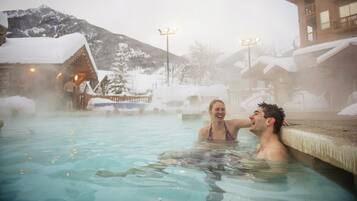 Relax in a serene hot spring surrounded by a wooden cabin and breathtaking mountain views.