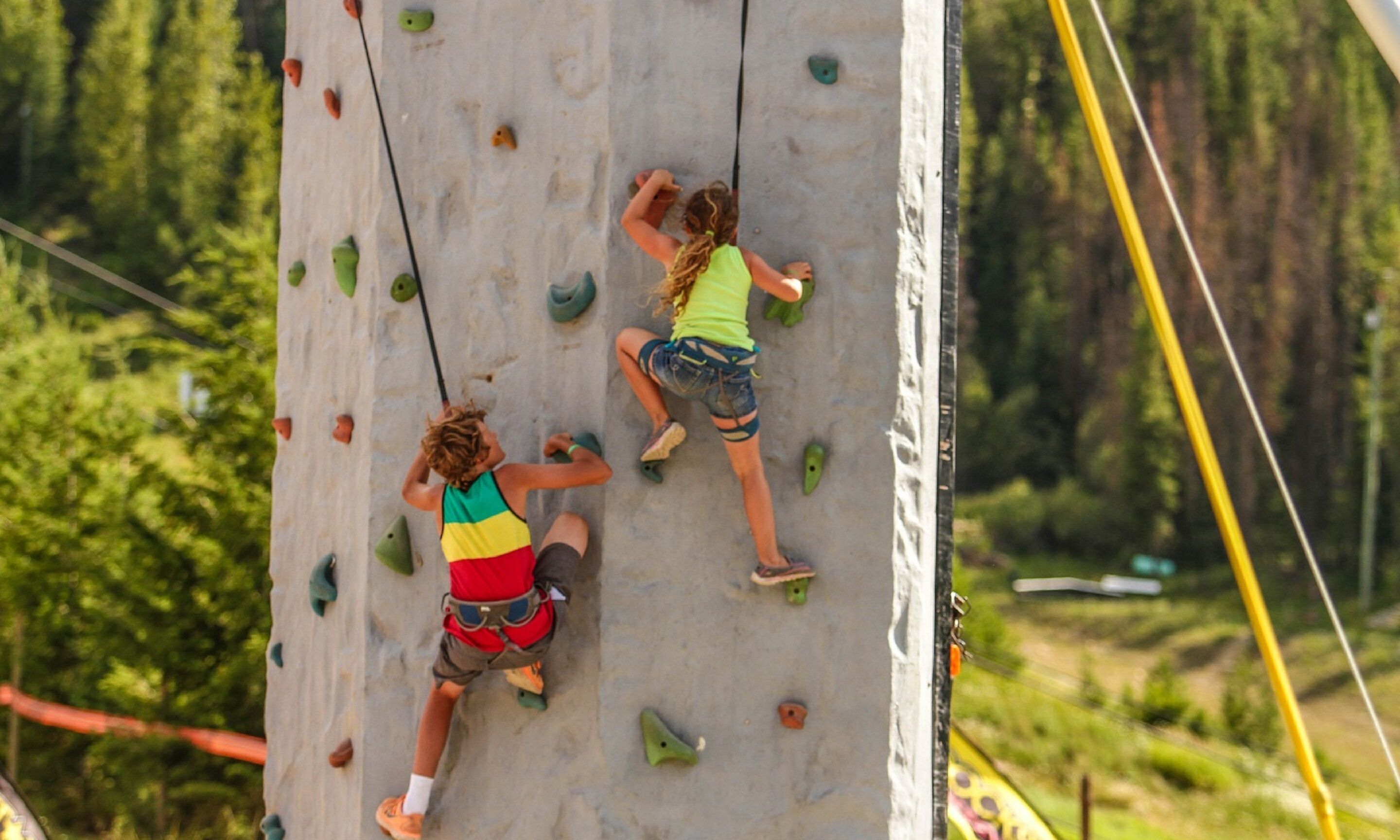 Two individuals climbing a rock wall with climbing holds.
