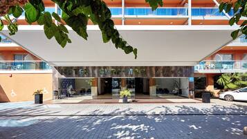 Entrada de hotel con diseño moderno, que cuenta con un amplio muro de vidrio, una zona de recepción con asientos y una entrada accesible para sillas de ruedas.
