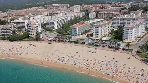 Un paisaje urbano costero con una playa extensa llena de gente y sombrillas, rodeado de edificios residenciales altos.