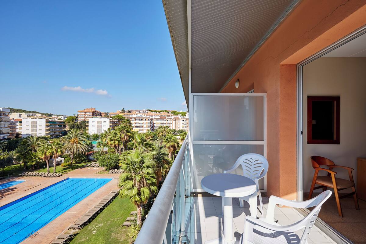 Un balcón con barandilla de vidrio, una piscina y una mesa con sillas.