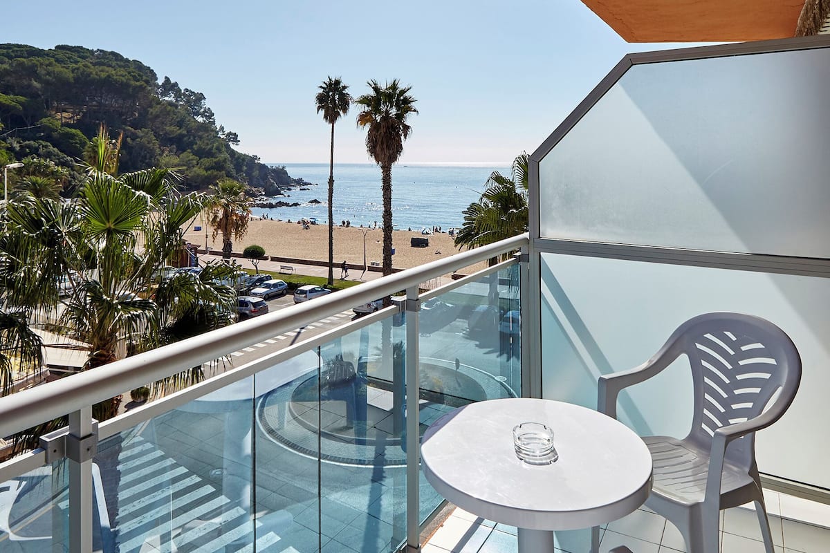 Un balcón con piscina de cristal, una mesa y sillas, con vista a una playa y al océano.