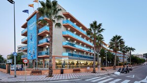Un hotel de varios pisos con balcones, palmeras y pavimento a cuadros.