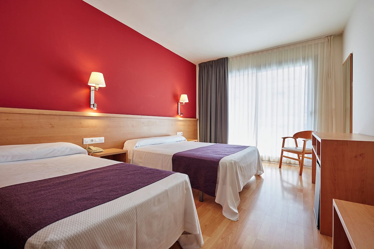 Habitación de hotel con dos camas, un escritorio, una silla y una ventana con cortinas.