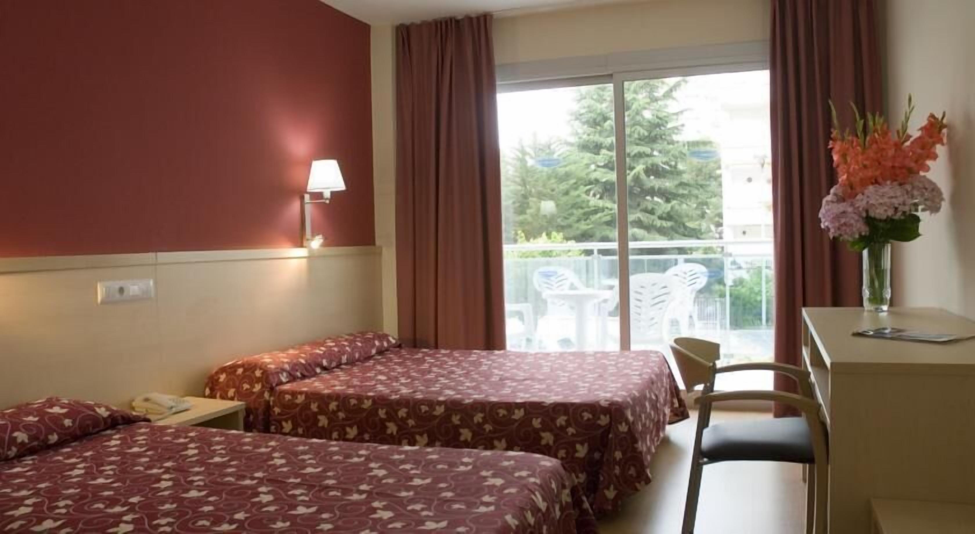 Habitación de hotel con dos camas, un escritorio, una silla, una lámpara y vistas al exterior.