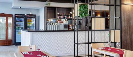 A modern restaurant interior with wooden tables, red tablecloths, and a bar area with various bottles and glasses.