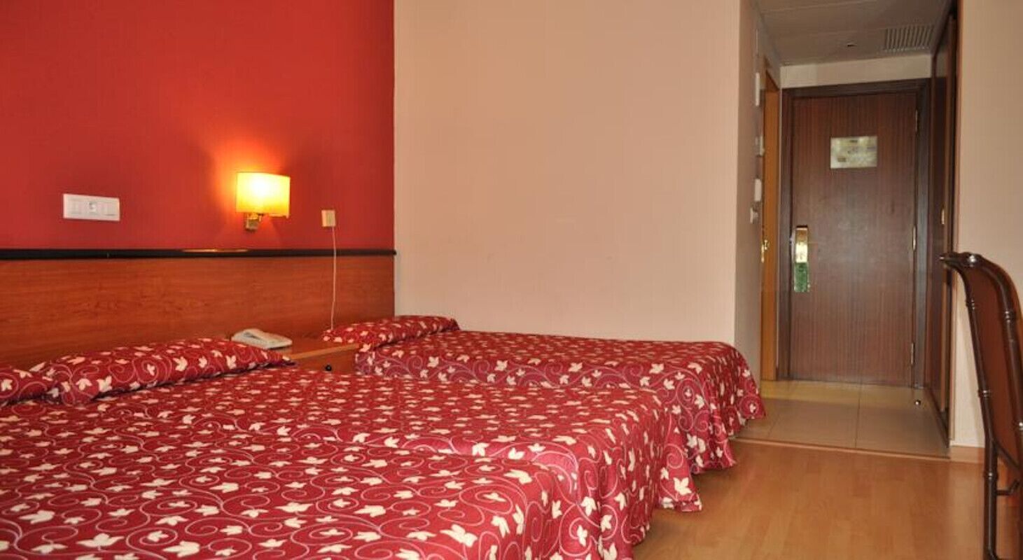 Habitación de hotel con dos camas, cabecero de madera, lámpara de pared y una puerta.