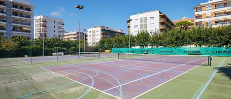 Una cancha de tenis al aire libre con una red, rodeada de edificios y árboles.