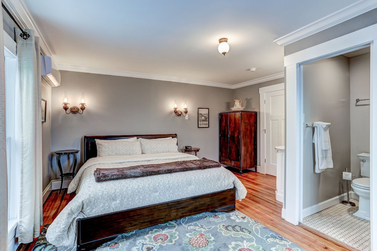 A bedroom with a large bed, a wooden wardrobe, and a bathroom with a toilet and sink.