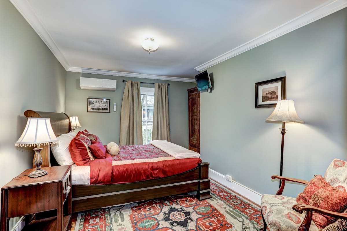 A bedroom with a bed, nightstands, a chair, a lamp, and a large window with curtains.