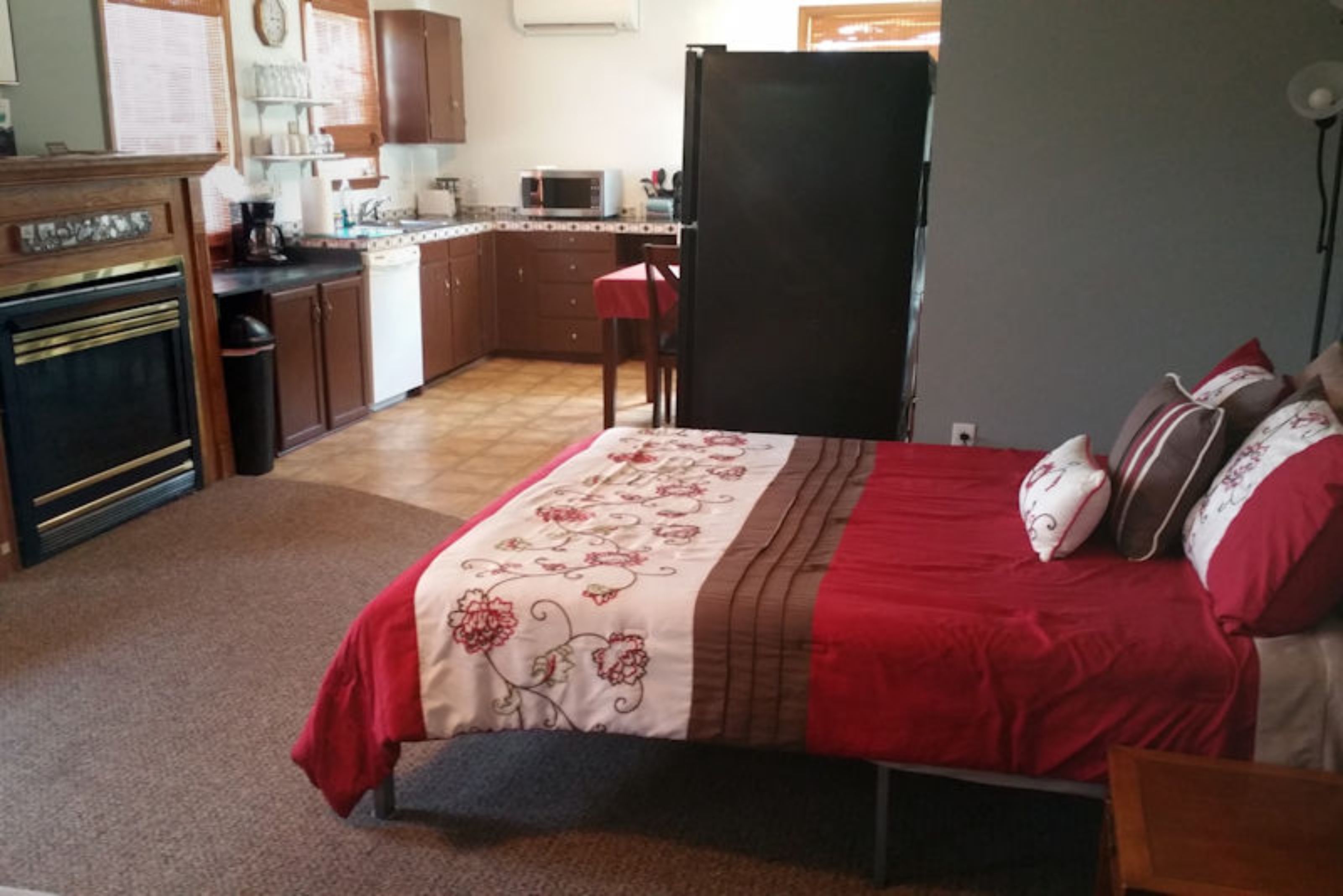 Un dormitorio con una cama, un edredón floral rojo y blanco, y una manta roja.