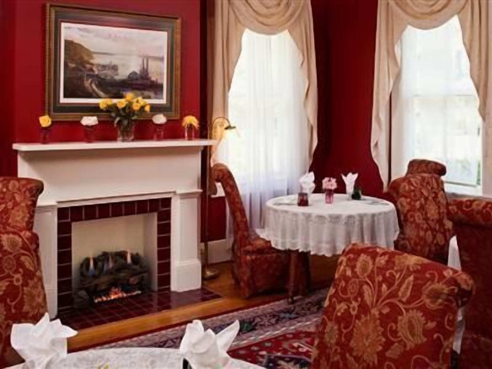 A room with a fireplace, red walls, and patterned chairs around a round table with a white tablecloth.