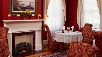 A room with a fireplace, red walls, and patterned chairs around a round table with a white tablecloth.