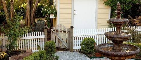 A garden with a white picket fence, a wooden deck, and a stone fountain.