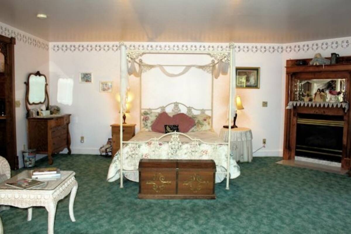 Un dormitorio con una cama con dosel, un aparador de madera, una mesita redonda con lámpara y una chimenea.