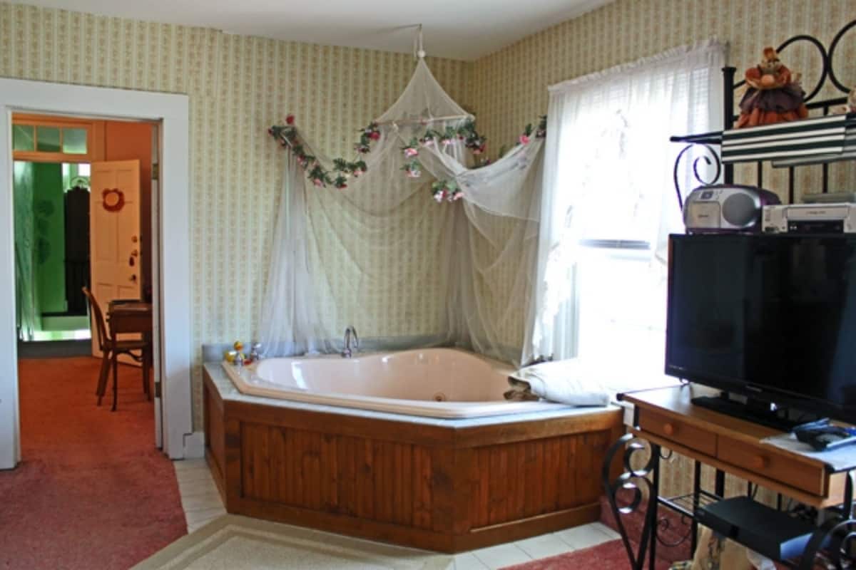 Un baño con una bañera de madera, un tocador con espejo y un televisor sobre un soporte de madera.