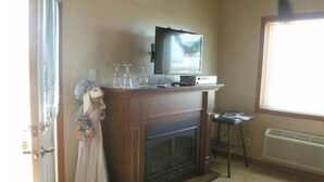Una sala de estar con chimenea, un televisor sobre un mueble bajo, una ventana con persianas y un peluche apoyado contra la pared.